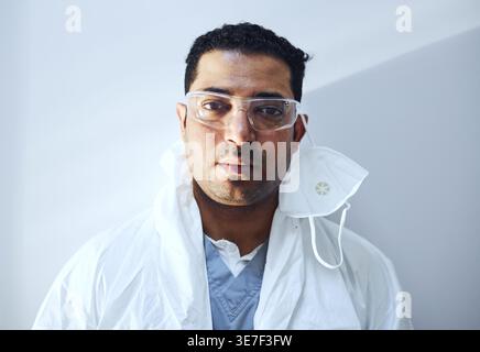 Middle Eastern male doctor wearing protective gear standing against wall in hospital Stock Photo