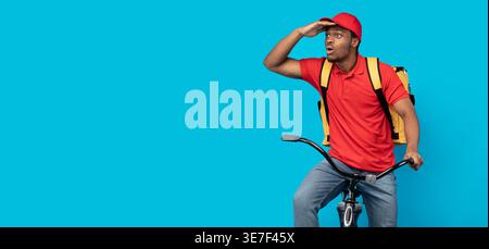 Black man looking away with hand on forehead sitting on bicycle against blue background in studio Stock Photo