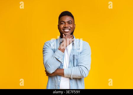 Black man touching his chin standing with crossed arms against yellow background in studio Stock Photo