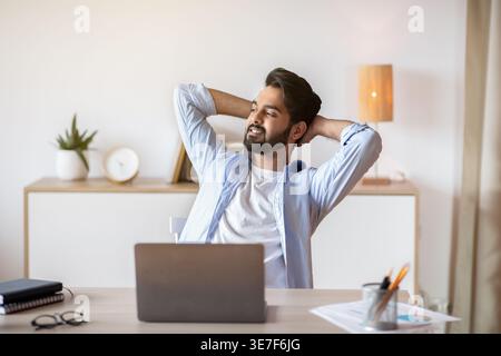 Relaxed Eastern Man Leaning Back In Chair, Resting After Online Work With Laptop, Millennial Arab Guy Sitting At Table With Computer In Home Office Wi Stock Photo