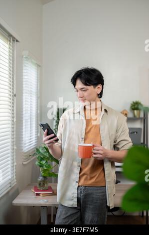 Thai businessman using smLifestylephone holding cup of coffee while standing in office Stock Photo