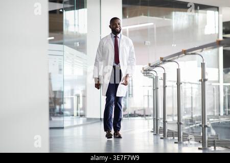 Bearded Black male scientist in white robe holding tablet walks into research center Stock Photo