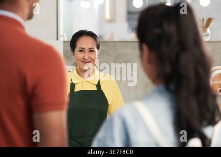 Smiling Asian female barista greeting customers in coffee shop Stock Photo