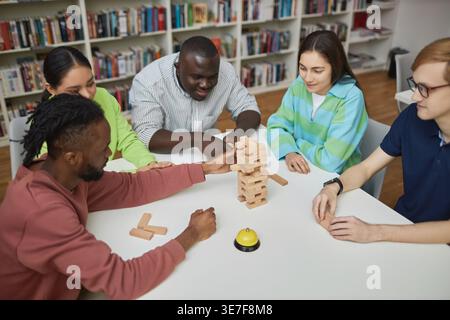 Diverse group of friends playing jenga while sitting together at table in college library Stock Photo