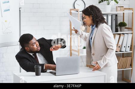 Frustrated Black female boss scolding male subordinate for making mistake in business project in office Stock Photo