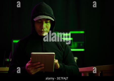Portrait of hacker using application on tablet computer when launching cyberattack Stock Photo