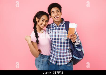 Cheerful Black couple holding passport with plane ticket standing against pink background in studio Stock Photo
