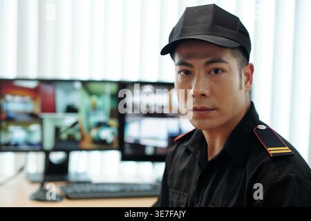 Asian male security guard sitting at table near computer in security office Stock Photo