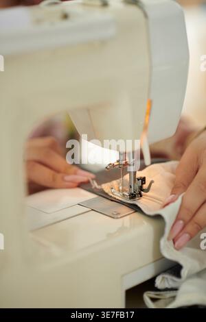 Hands of Asian seamstress sewing fabric using electric sewing machine sitting at table in atelier Stock Photo