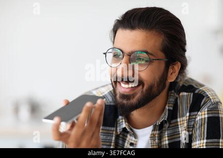 Arab man wearing eyeglasses having phone call looking away while standing at home Stock Photo