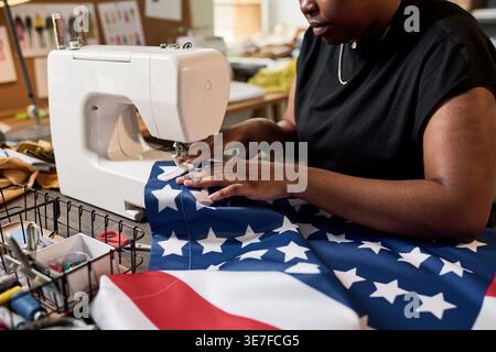 Cropped image of Black woman sewing American flag using electric sewing machine sitting in tailor shop during daytime Stock Photo