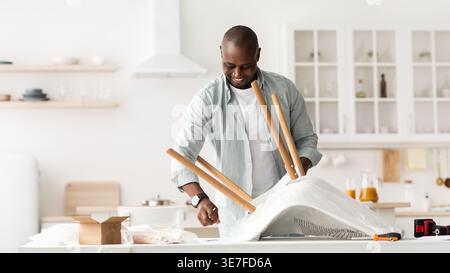Black man assembling chair standing in kitchen at home Stock Photo