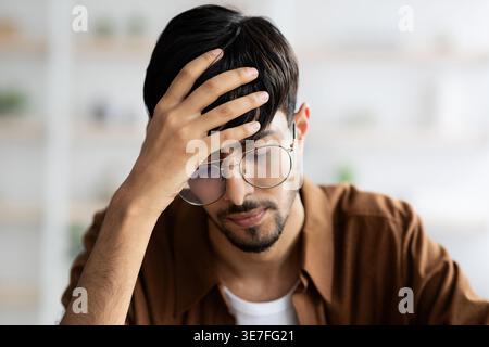 Middle Eastern man wearing eyeglasses touching his head while sitting at home Stock Photo