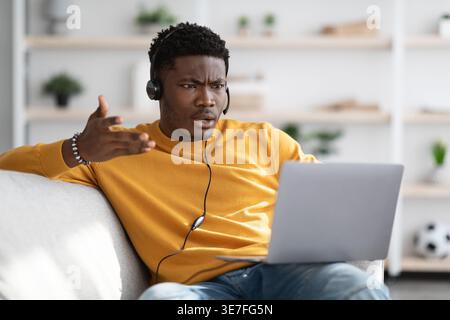 Black man in headset having video call using laptop while sitting on sofa at home Stock Photo