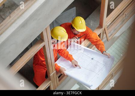 Asian and mixed race male construction workers discussing house plan while standing in construction site Stock Photo