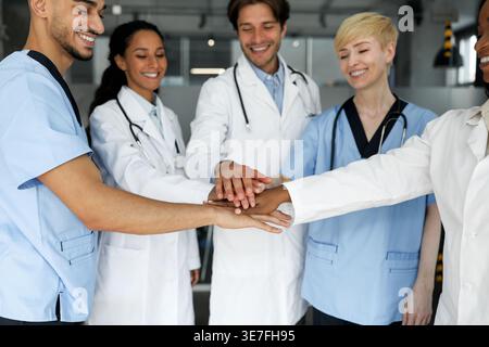Diverse group of doctors putting their hands together while standing in hospital Stock Photo
