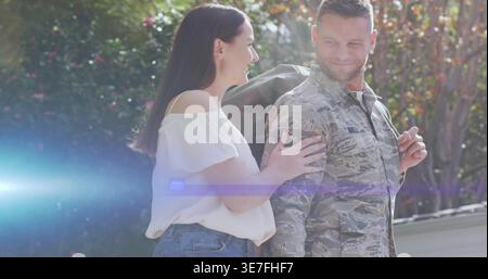 Couple standing in yard, man in camouflage uniform with duffel, woman in white blouse touching arm Stock Photo