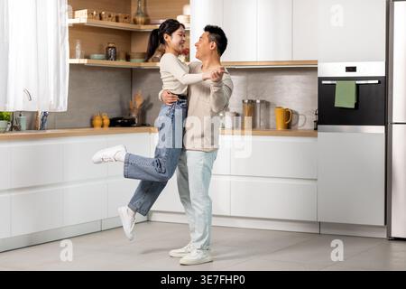 Cheerful Asian couple having fun dancing together in kitchen at home Stock Photo