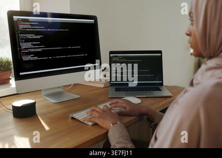 Black female programmer in hijab working codes on computer while sitting at table at home office Stock Photo