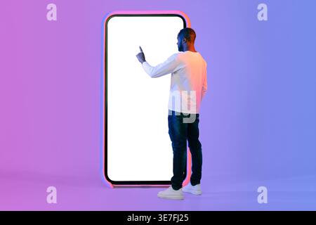 Smiling Black man using huge smartphone while standing in front of purple wall in studio with neon lights Stock Photo