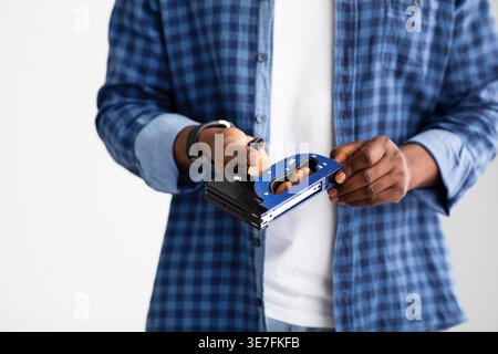 Cropped image of Black man holding industrial stapler standing against white wall at home Stock Photo