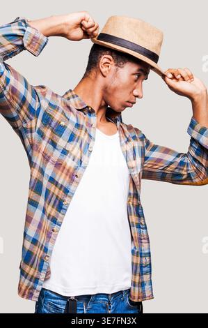 Black man looking sideways tipping straw hat while standing against light gray background Stock Photo