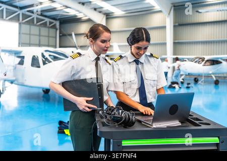 Middle Eastern female pilot using laptop standing beside her co-pilot in hangar Stock Photo