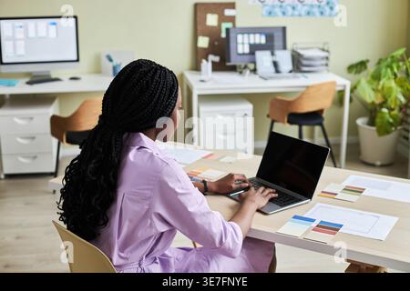 Black female designer working on laptop while sitting at table in office Stock Photo