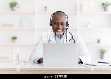 Black male doctor wearing headset talking to his patient while sitting at desk in clinic Stock Photo