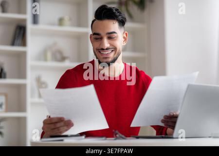 Arab man working on documents sitting at desk with laptop at home Stock Photo