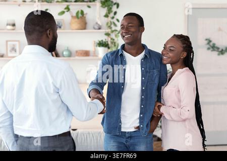 Black male psychologist and Black couple standing and shaking hands after successful therapy session in office Stock Photo