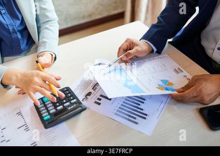 Asian managers using calculator analyzing various reports sitting at table in office during daytime Stock Photo