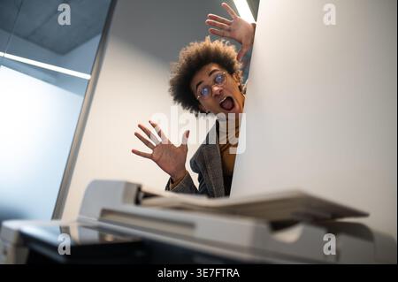 Black businessman with afro wearing eyeglasses standing behind printing machine in office Stock Photo