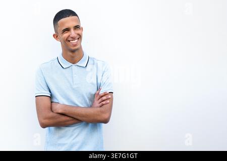 Smiling Arab male with crossed arms standing against white wall during daytime Stock Photo
