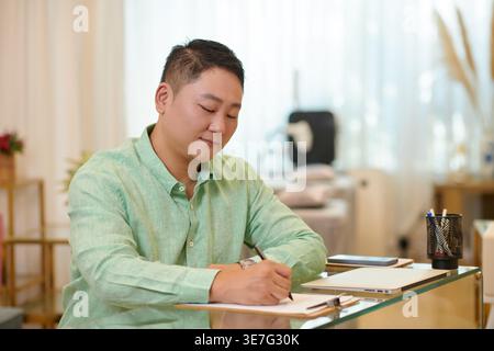 Asian businessman writing on document sitting at table in salon Stock Photo