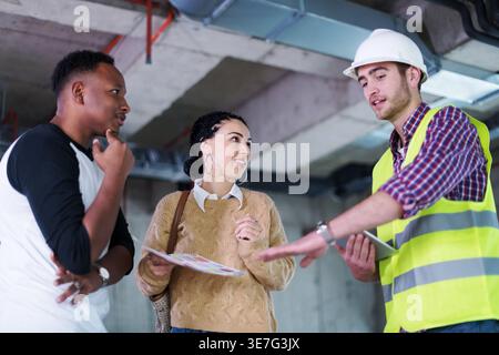 Middle Eastern woman and Black man standing and talking to caucasian male architect explaining plans inside the building Stock Photo