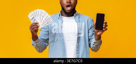 Cropped image of surprised Black man holding smartphone and cash standing against yellow background in studio Stock Photo