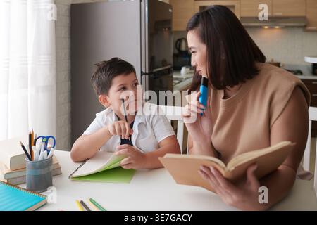 Focused Asian mother with highlighter helping her Mixed race son to do homework sitting at table in dining room at home Stock Photo