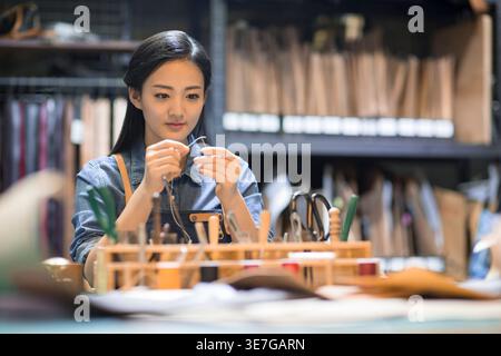 Chinese leather craftswoman sitting at table working in workplace Stock Photo