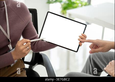 Asian business woman discussing and showing some details on tablet to male colleague in office Stock Photo