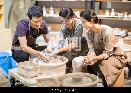 Chinese male and female potter working on potters wheel making ceramic pot from clay in pottery workshop Stock Photo