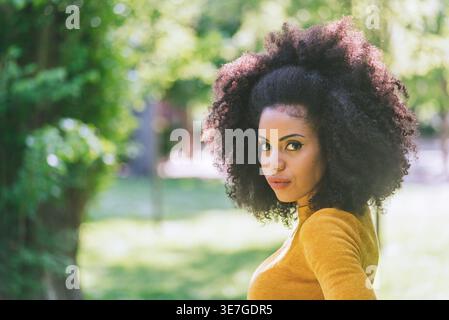 Hispanic female with curly hair looking sideways standing in park during daytime Stock Photo