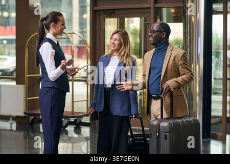 Black man and caucasian woman guest talking to female staff standing in hotel lobby Stock Photo