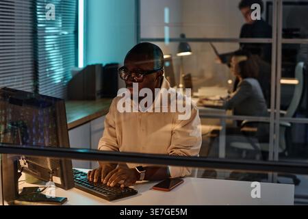 Focused Black male programmer in eyeglasses examining computer codes working overtime in office Stock Photo
