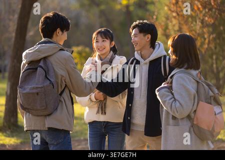 Smiling Chinese male college students with backpack shaking hands standing with female classmates on campus at sunset Stock Photo