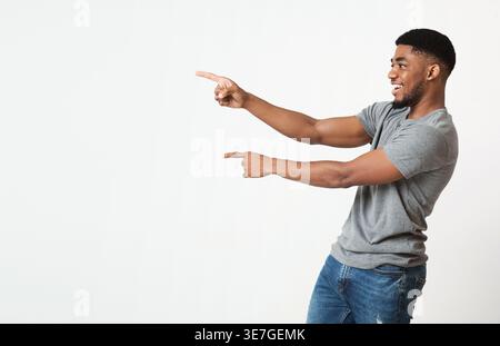 Great promo. Excited african-american man pointing two fingers aside at copy space, white studio background Stock Photo