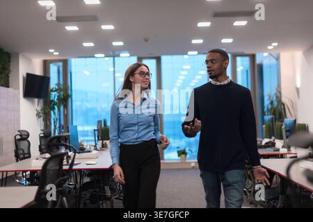 Black male and caucasian female office workers talking while walking in office Stock Photo