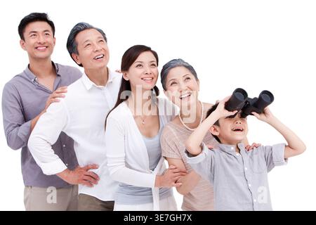 Smiling Chinese boy looking at the view using binoculars while standing with his family against white background in studio Stock Photo