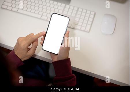 Man wearing maroon hoodie using smartphone while sitting at table in office Stock Photo