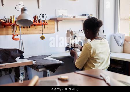 Black woman Lifestyleisan sewing leather using machine sitting in workshop Stock Photo